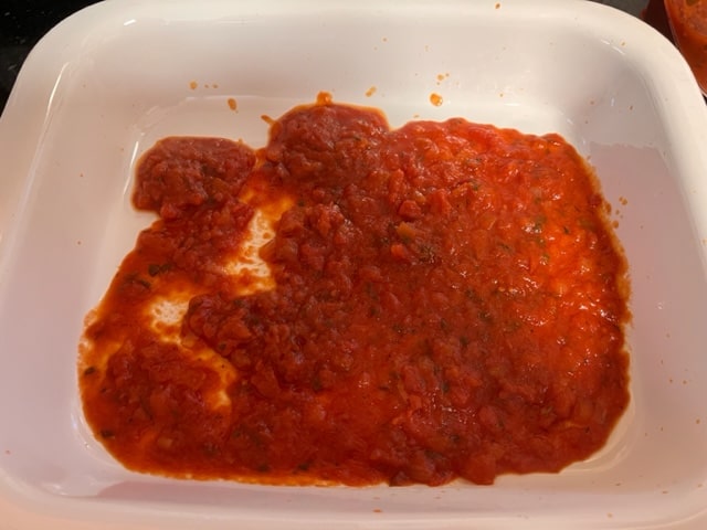 putting sauce on the bottom of lasagna pan