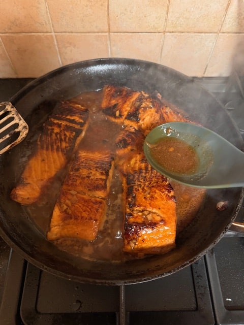 spooning marinade over cooking fish