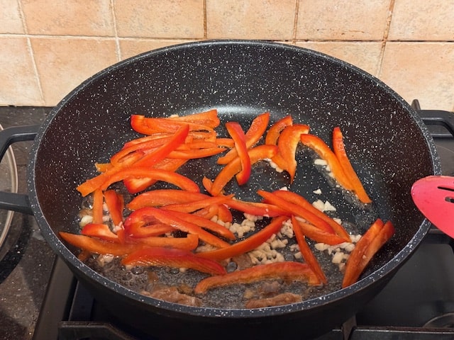 sliced peppers and garlic in pan with onions