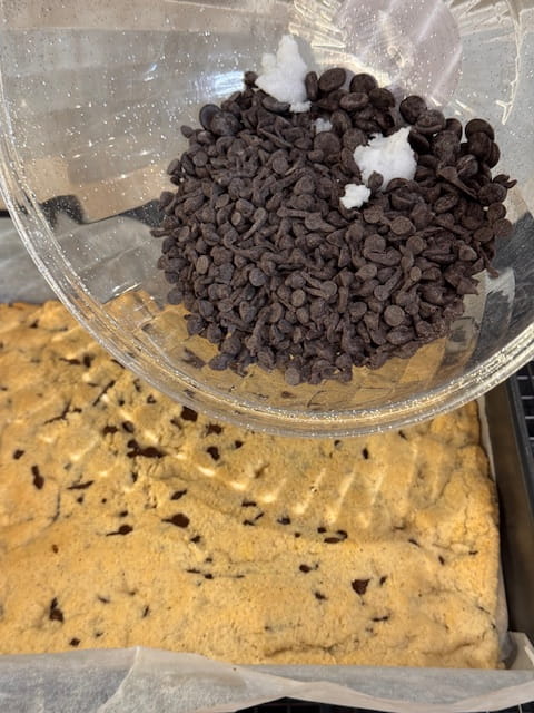 pouring chocolate chips and coconut oil on baked bars